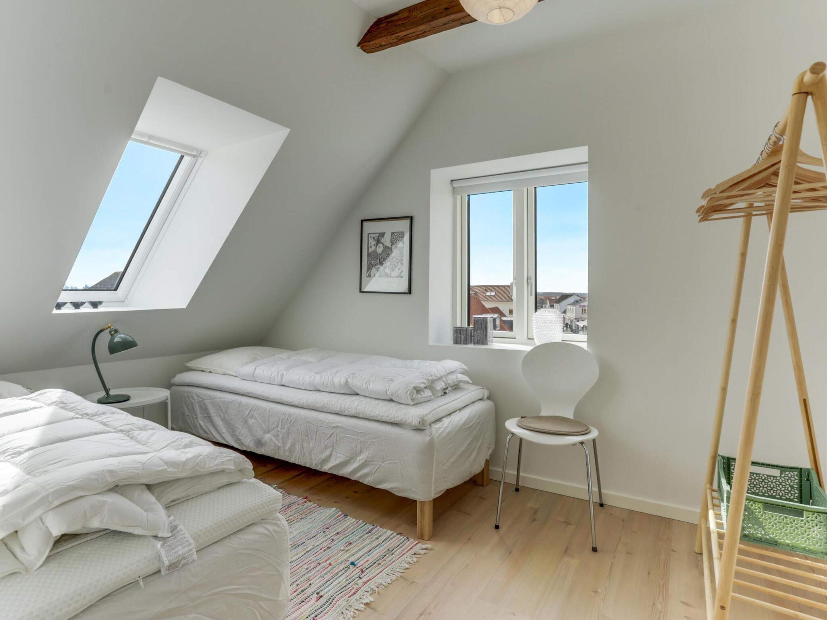 Quarto com teto inclinado, cama, poltrona, escrivaninha e cabideiro.