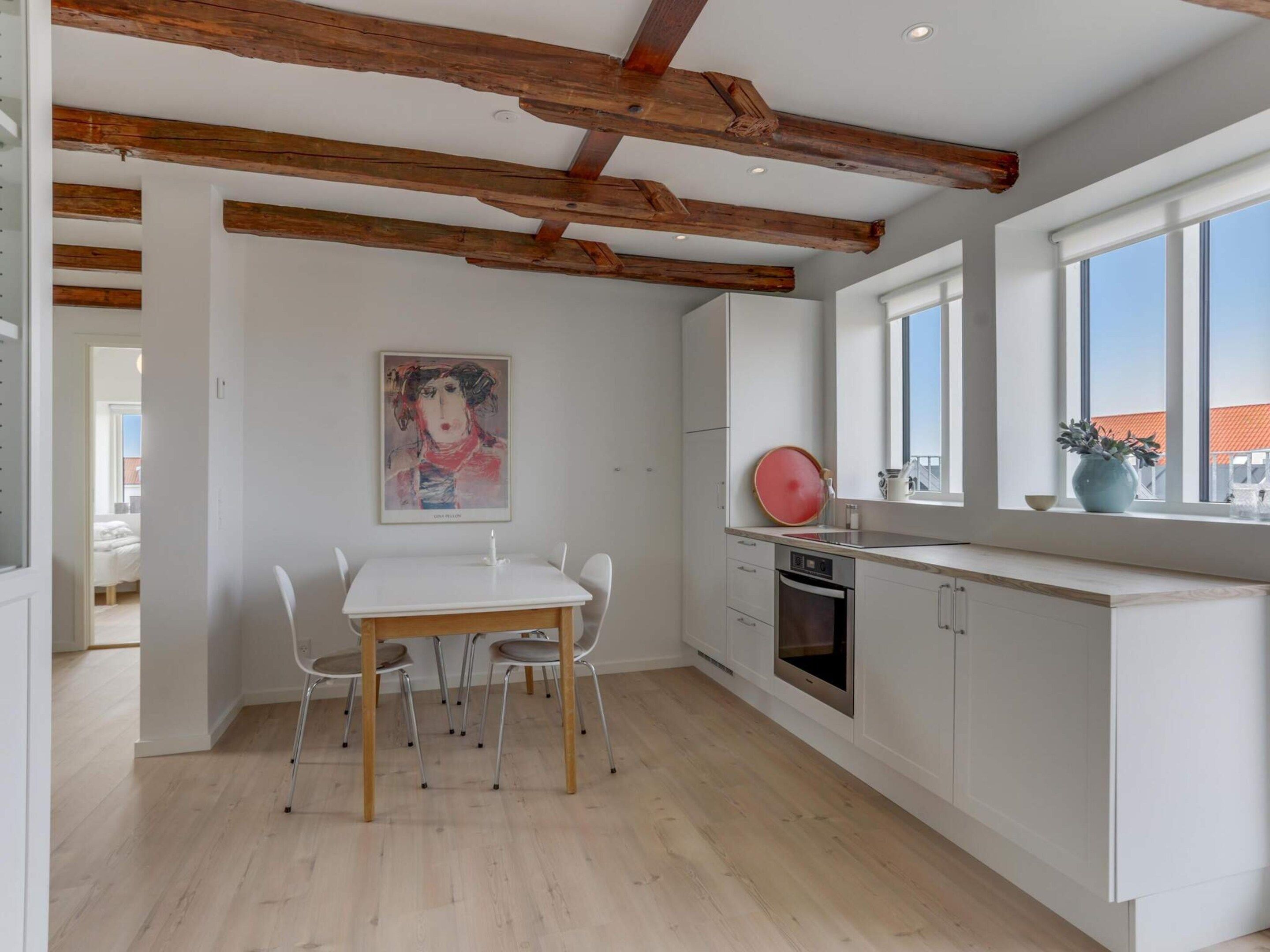 A modern kitchen with white cabinets, a wooden ceiling, and a dining area with a table and chairs.