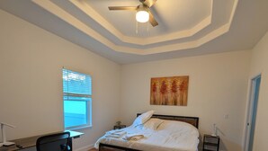 Un dormitorio con cama, escritorio, silla, ventilador de techo y ventana.