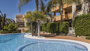 A swimming pool with a tiled edge, surrounded by palm trees and a building with balconies. - La Palmera (Javea / Xàbia)