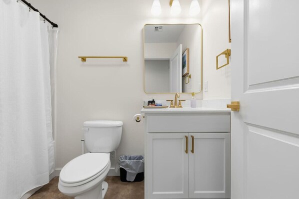 Une salle de bain avec des toilettes blanches, un lavabo avec un robinet doré, un miroir et un porte-serviettes.