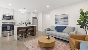 Eine moderne Küche mit weißen Schränken, einer zentralen Kochinsel mit Sitzgelegenheiten, einem grauen Sofa, einem runden Couchtisch und einem Gemälde an der Wand.