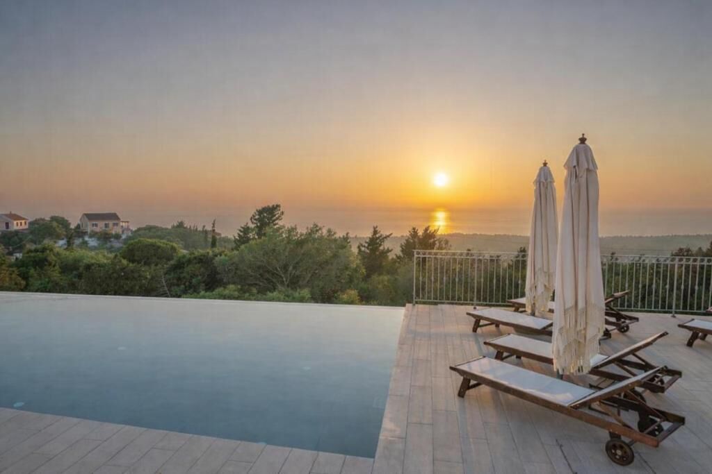 An outdoor swimming pool with lounge chairs and umbrellas, overlooking a sunset view.