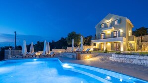 A modern two-story house with a swimming pool, lounge chairs, and a stone wall. - HELLOSUMMER (Kefalonia)