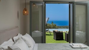 A bedroom with a bed, white pillows, a view of the ocean through a sliding door, and a wicker lamp. - HELLOSUMMER (Kefalonia)