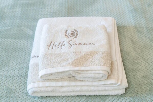A folded white towel with 'Hello Summer' and a laurel wreath logo on a textured surface. - HELLOSUMMER (Kefalonia)