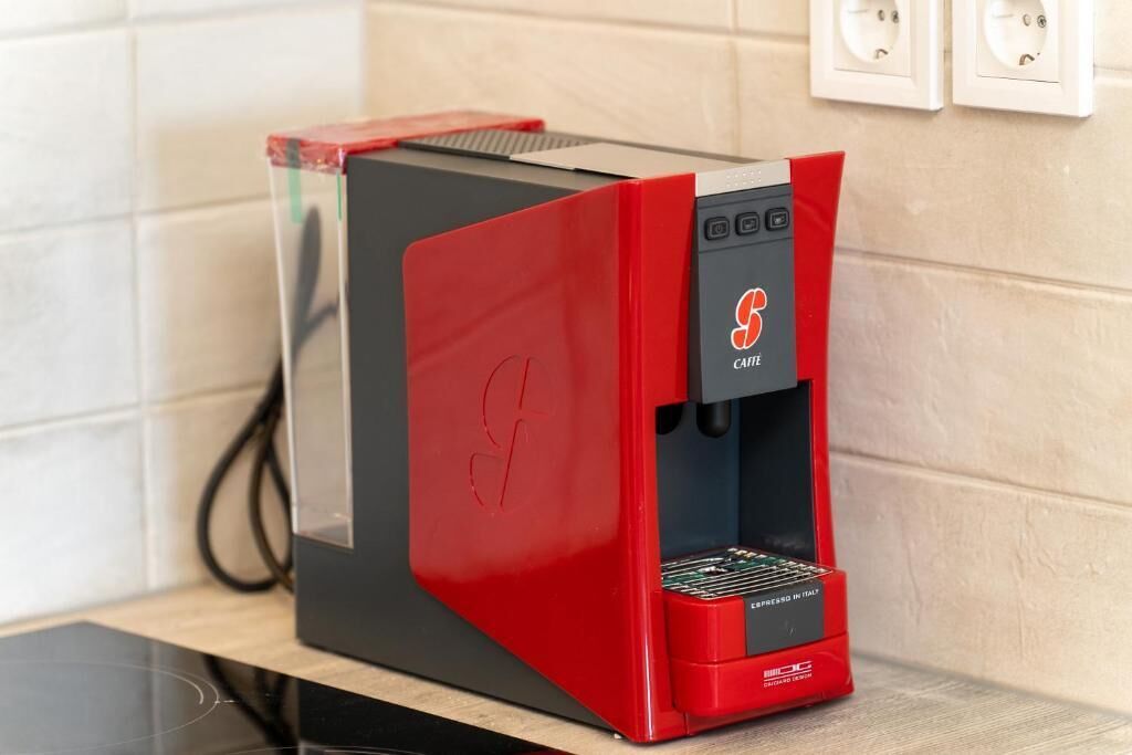 Een rode en zwarte koffiemachine met een logo, op een aanrecht geplaatst.