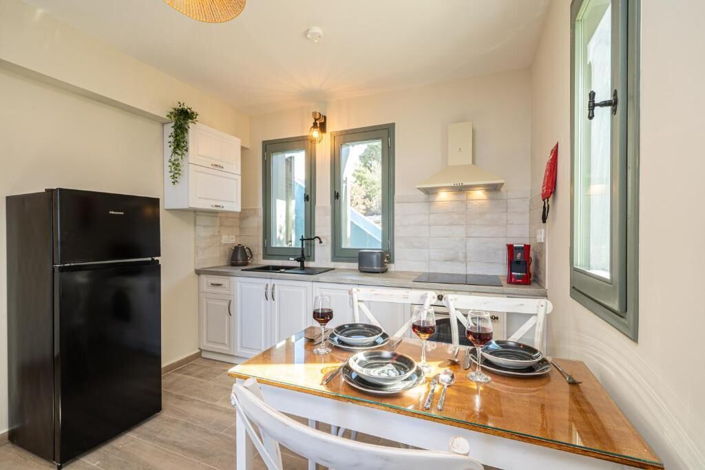 A modern kitchen with a black refrigerator, white cabinets, a wooden dining table, and a window with a view.