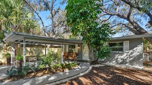 Una casa moderna con un porche cubierto, un jardín ajardinado y un gran árbol.