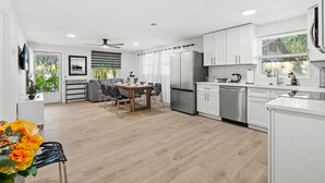 Una cocina moderna con armarios blancos, electrodomésticos de acero inoxidable y una zona de comedor con una mesa y sillas.