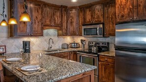 Una cocina con armarios de madera, encimeras de granito, electrodomésticos de acero inoxidable e iluminación colgante.