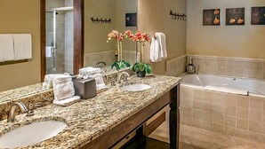 Un baño con encimera de granito, lavabo, espejo, ducha y bañera. Hay toallas y una planta en maceta sobre la encimera.