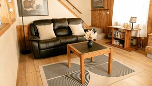 A cozy living room with a black leather sofa, a wooden coffee table, and a bookshelf. - 3 bedroom Townhome in West Yellowstone, perfect for families!!! (West Yellowstone)