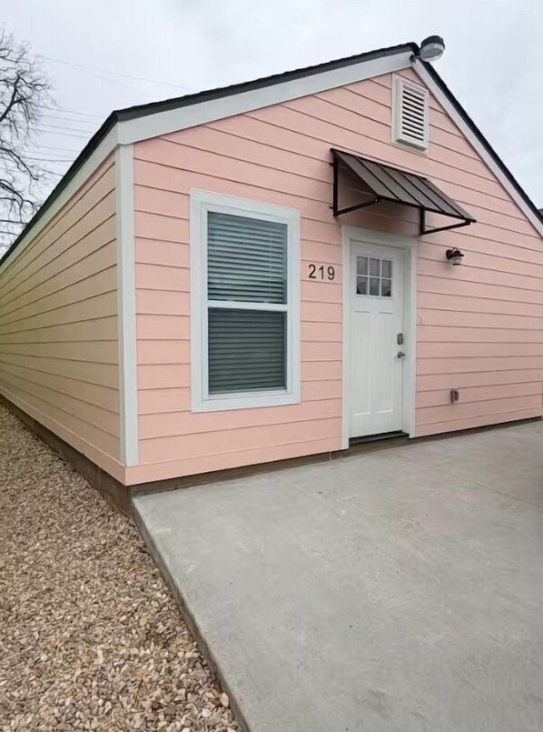 A pink building with a white door, a window with blinds, and the number 219.