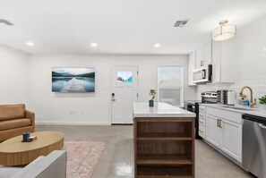 A modern kitchen with white cabinets, a central island, and a dining area with a brown sofa and a round coffee table.