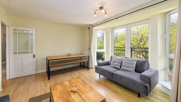 Una habitación con sofá, mesa de centro de madera, banco y puerta con paneles de vidrio esmerilado.