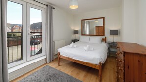 Un dormitorio con cama, cómoda, mesita de noche, espejo y ventana con cortinas.