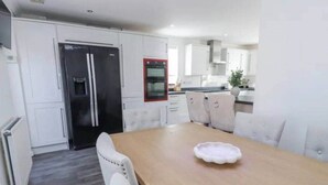 Uma cozinha moderna com armários brancos, uma ilha central e um espaço de refeições com mesa de madeira e cadeiras brancas.