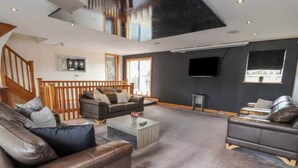 A spacious living area with a high ceiling, a staircase, and a flat-screen TV mounted on the wall. - Penthouse apartment in the heart of towyn (Towyn)