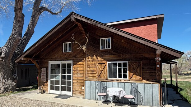 A wooden cabin with a red roof, a porch with two chairs, and a table. - Jill's place is Cozy 2 bedroom cottage on a quiet dead end road, near Cortez. (Cortez)