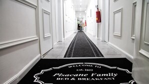 Un couloir recouvert d’une moquette noire mène à une porte sur laquelle on peut lire : « Bienvenue à la maison d’hôtes familiale Pisacane, à Naples. »