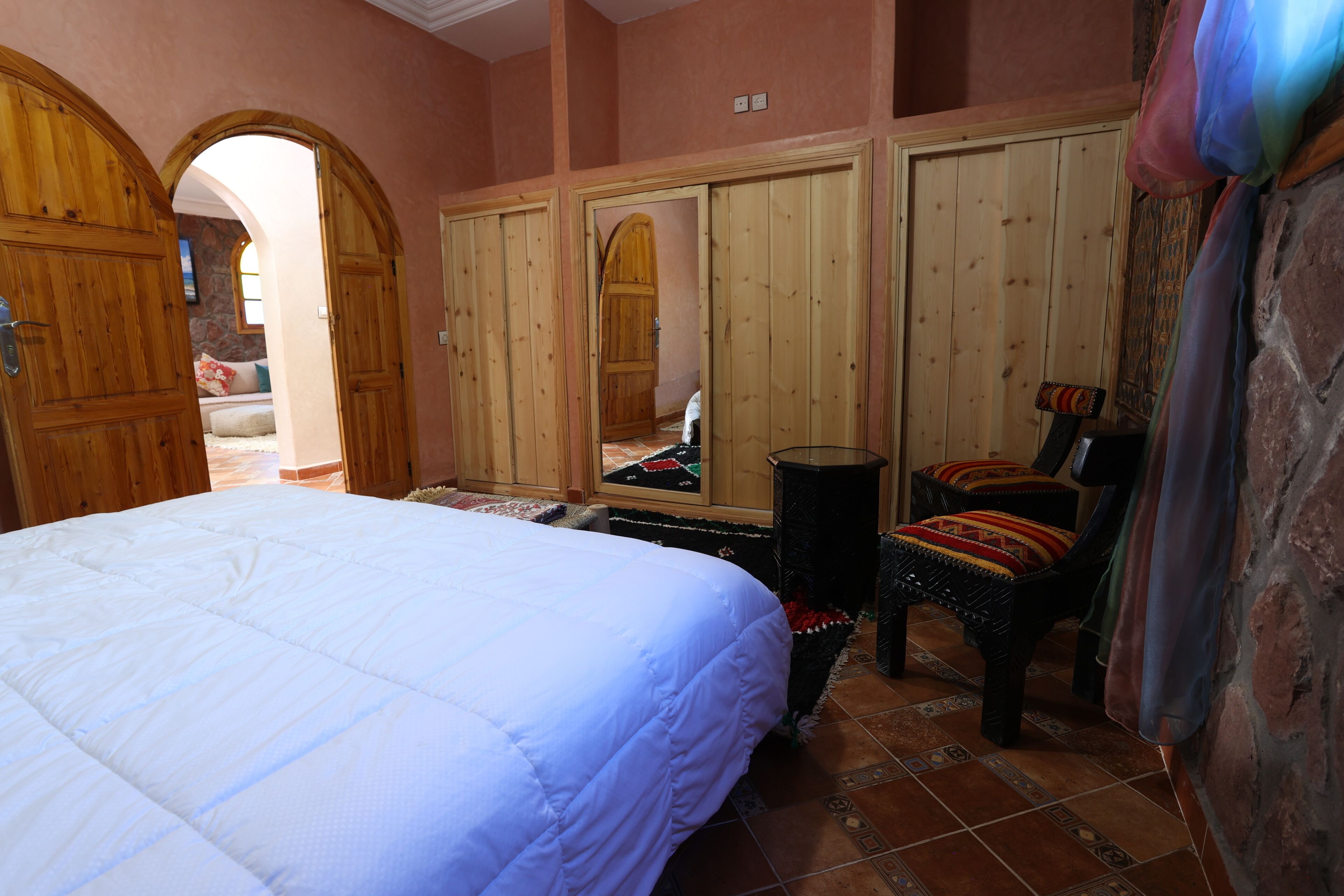 Une chambre avec un grand lit, une armoire en bois et une chaise avec un coussin.