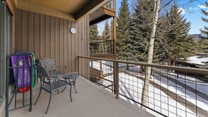 A balcony with a view of snow-covered ground and trees, a metal railing, and a table with chairs. - Lodgepole #2020 (Keystone)