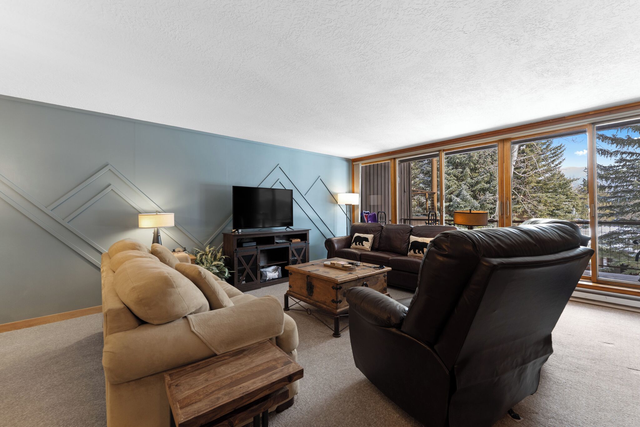 A living room with a sofa, armchair, TV, and a large window with a view of trees.