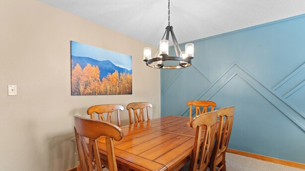 A dining area with a wooden table and chairs, a chandelier, and a mountain landscape painting on the wall. - Lodgepole #2020 (Keystone)