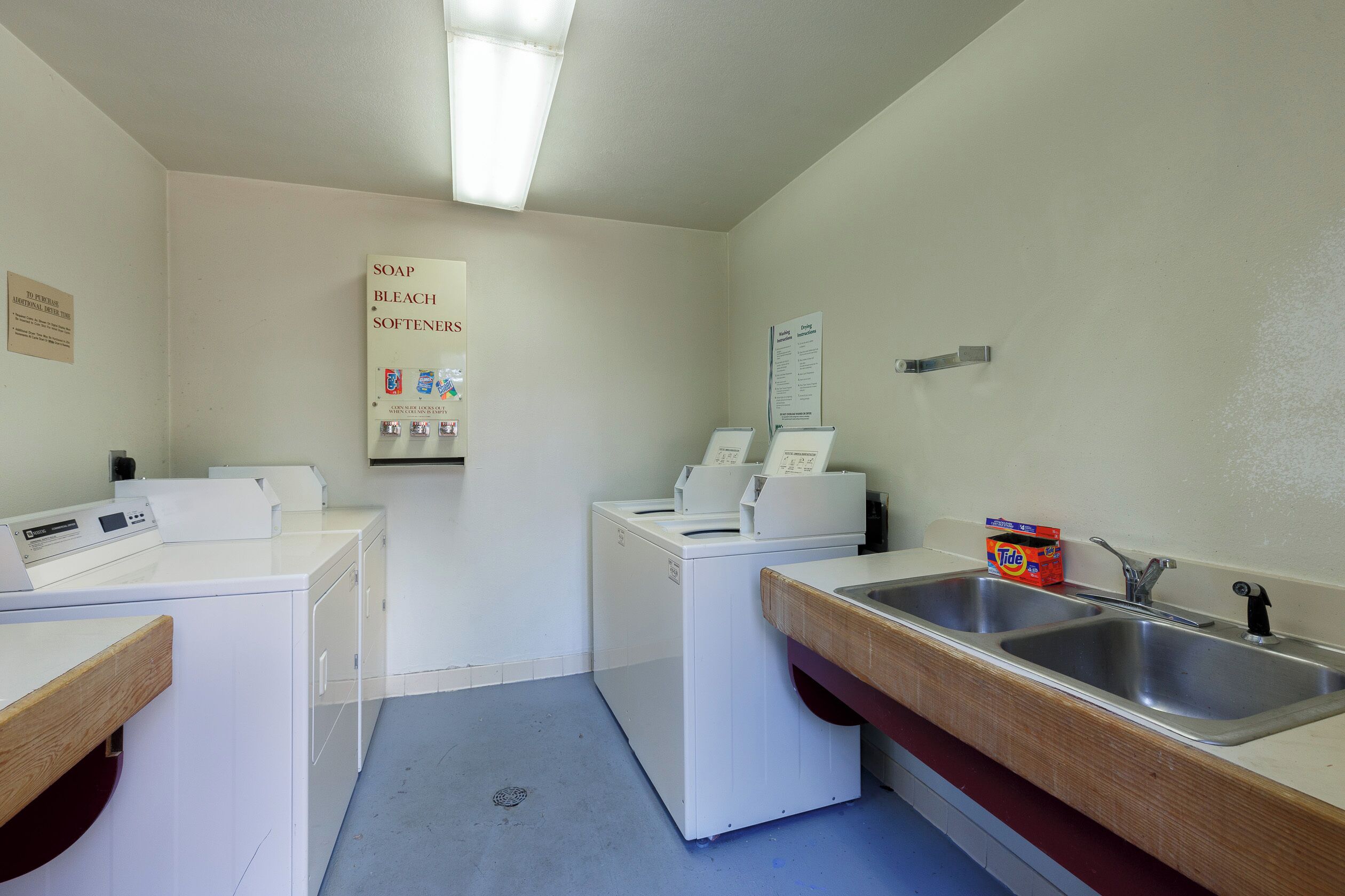 A laundry room with two washing machines, a sink, and a sign indicating additional purchase time for soap, bleach, and softeners.