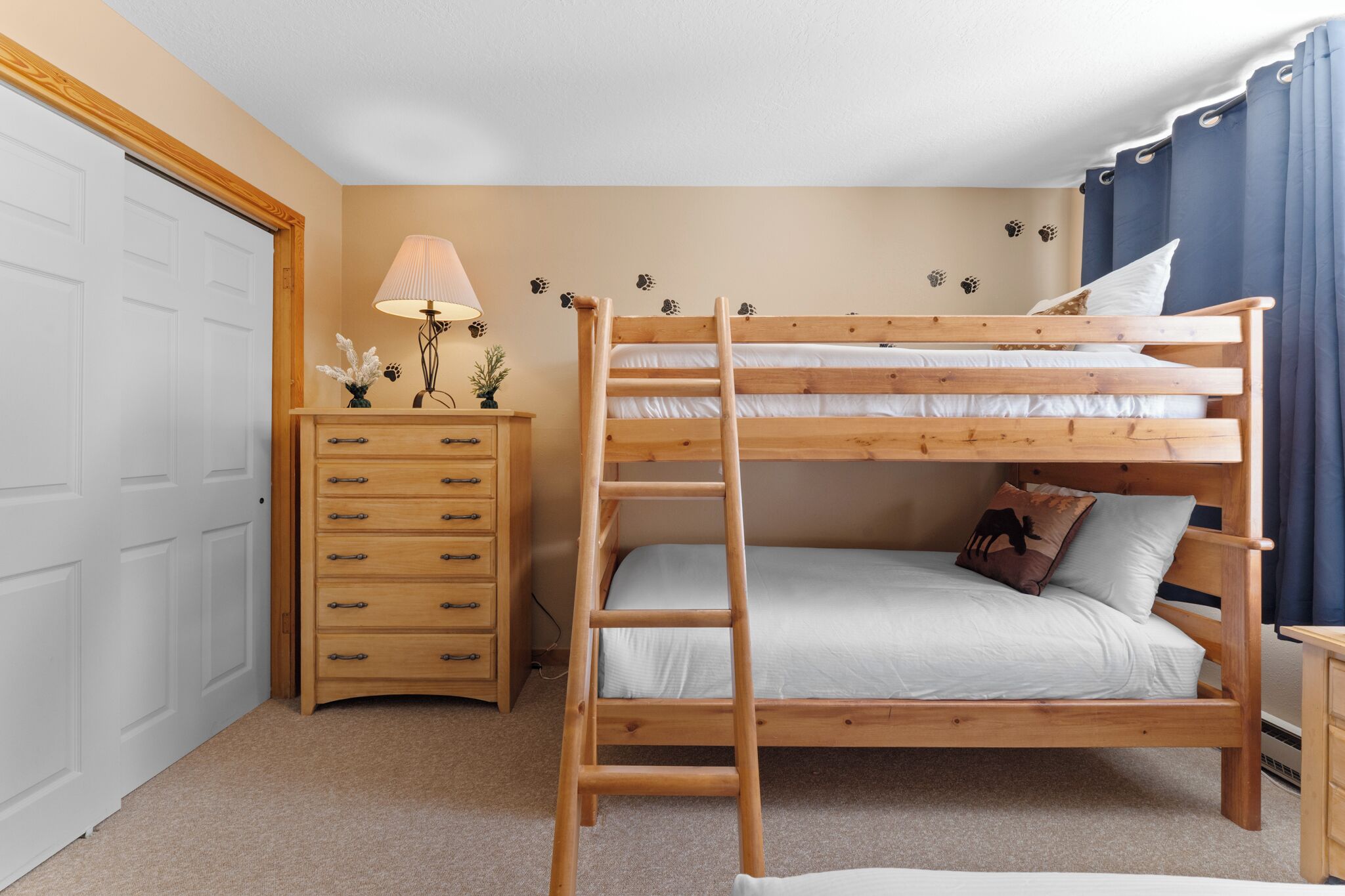 Ein Etagenbett mit einer Leiter, eine Holzkommode mit Schubladen, eine Lampe und Wanddekorationen.