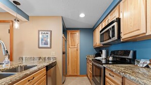 A kitchen with wooden cabinets, granite countertops, stainless steel appliances, and a poster on the wall. - Lodgepole #2020 (Keystone)