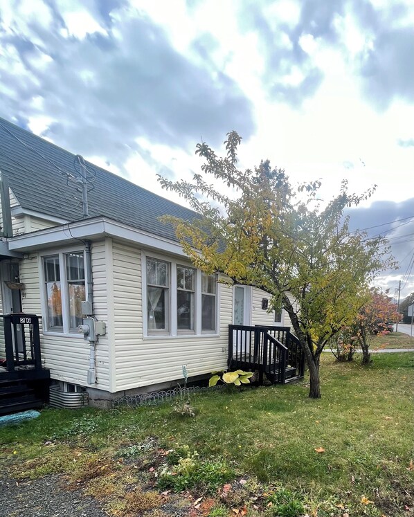 Ein eingeschossiges Haus mit Veranda, einem kleinen Baum und einem Rasengrundstück.