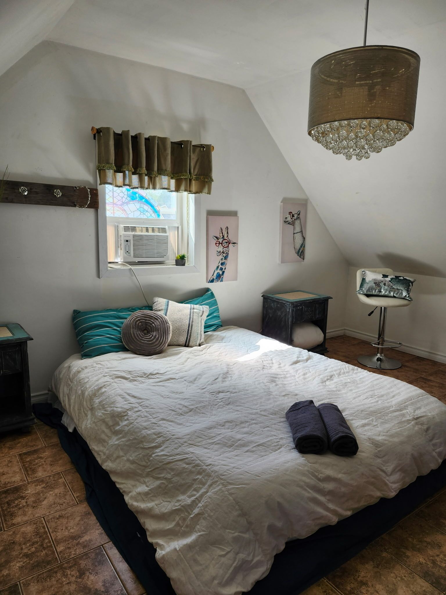 Una camera da letto con un letto grande, una finestra con tende, un lampadario, un condizionatore d'aria a parete e un tavolino con una sedia.