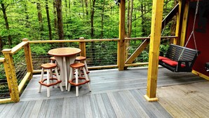 A wooden deck with a round table and stools, surrounded by a metal railing, overlooking a forest. - Family-Friendly Hidden Valley Cabin with Creek Views (Somerset)