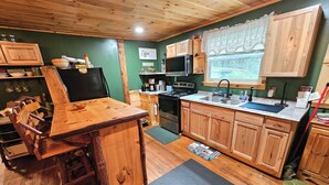 A rustic kitchen with wooden cabinets, a bar area, and a window with a view. - Family-Friendly Hidden Valley Cabin with Creek Views (Somerset)