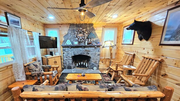 A log cabin interior with a stone fireplace, wooden furniture, and a mounted animal head. - Family-Friendly Hidden Valley Cabin with Creek Views (Somerset)