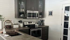 Une cuisine avec des meubles de couleur sombre, un four à micro-ondes, une cuisinière et un évier.