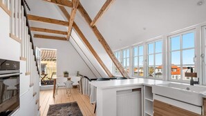 A modern kitchen with a sloped ceiling, wooden beams, and large windows. - 4 Star Holiday Home in Lokken (Lokken)