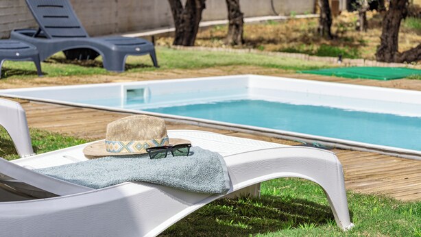 Zona de piscina con sillones de descanso y un sombrero sobre uno de ellos.