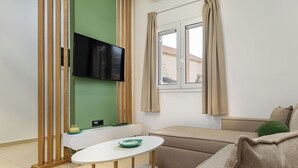Una sala de estar moderna con un televisor de pantalla plana montado en una pared verde, un sofá color crema, una mesita redonda con un tazón verde y una ventana con cortinas color crema.