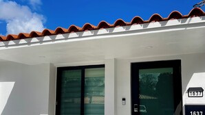Un edificio blanco con puerta y ventanas negras, techo de tejas y felpudo.