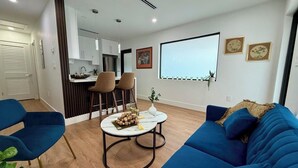 Una sala de estar moderna con un sofá azul, una mesa de centro con adornos, y una zona de cocina con armarios blancos y un taburete de bar.