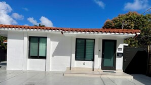 Una casa moderna con techo de tejas, dos ventanas con contraventanas y una puerta negra con placa numérica.