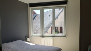 A bedroom with a bed, a window, a radiator, and a chair.