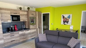 A modern living room with a grey sofa, a coffee machine, and a microwave in the kitchen area.