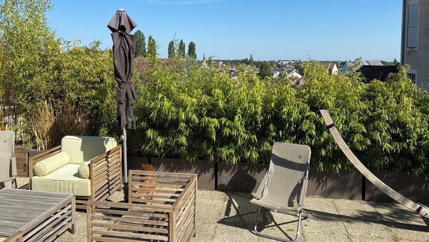 A patio with a sofa, a wooden chair, and an umbrella.