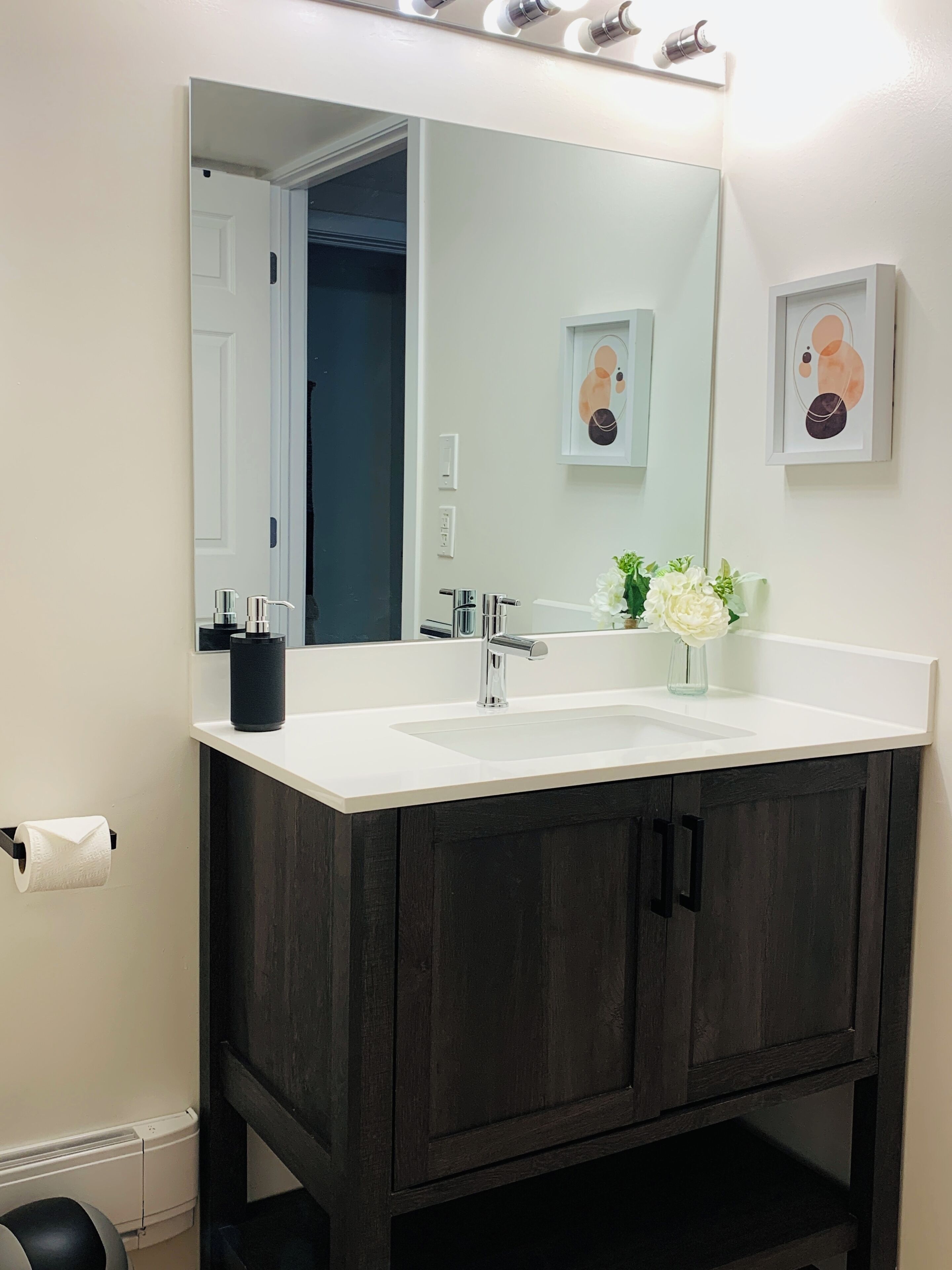 A bathroom with a white sink, dark wooden cabinets, a large mirror, and a framed picture on the wall.