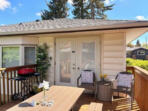 Une terrasse couverte avec une table, des chaises, un chariot-barbecue et un pot de fleurs.