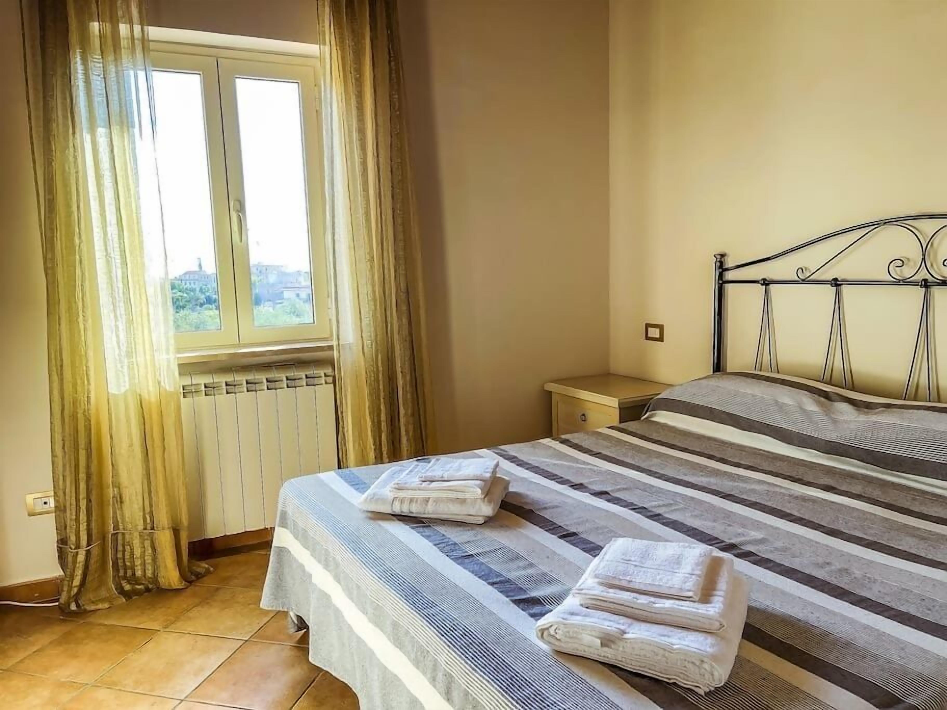 Una camera d'albergo con un letto, un comodino, una finestra con tende e un termosifone.